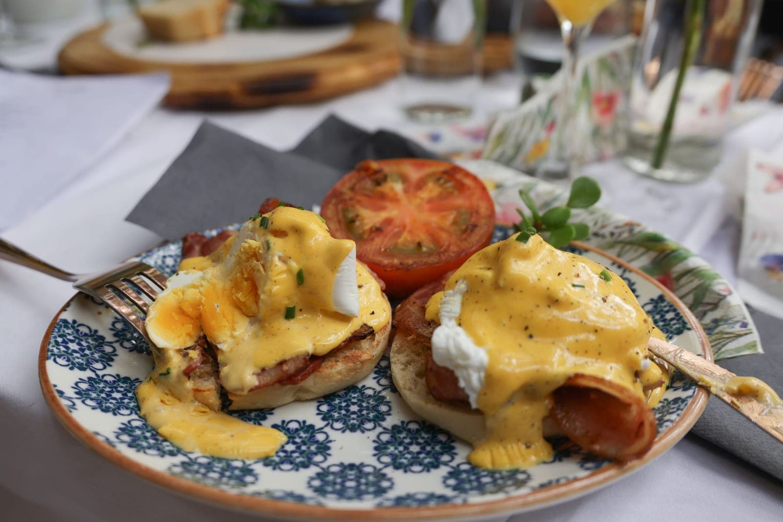 Two halves of eggs benedict under a thick pour of hollandaise, with a grilled tomato beside them