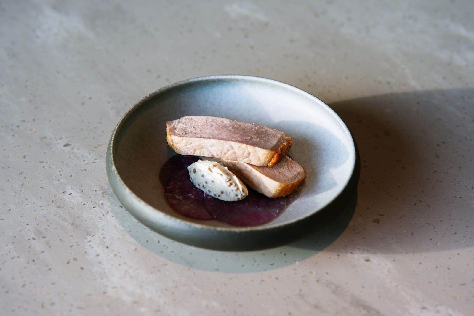 Slices of pale pink cooked duck breast on a ceramic plate with a dark sauce