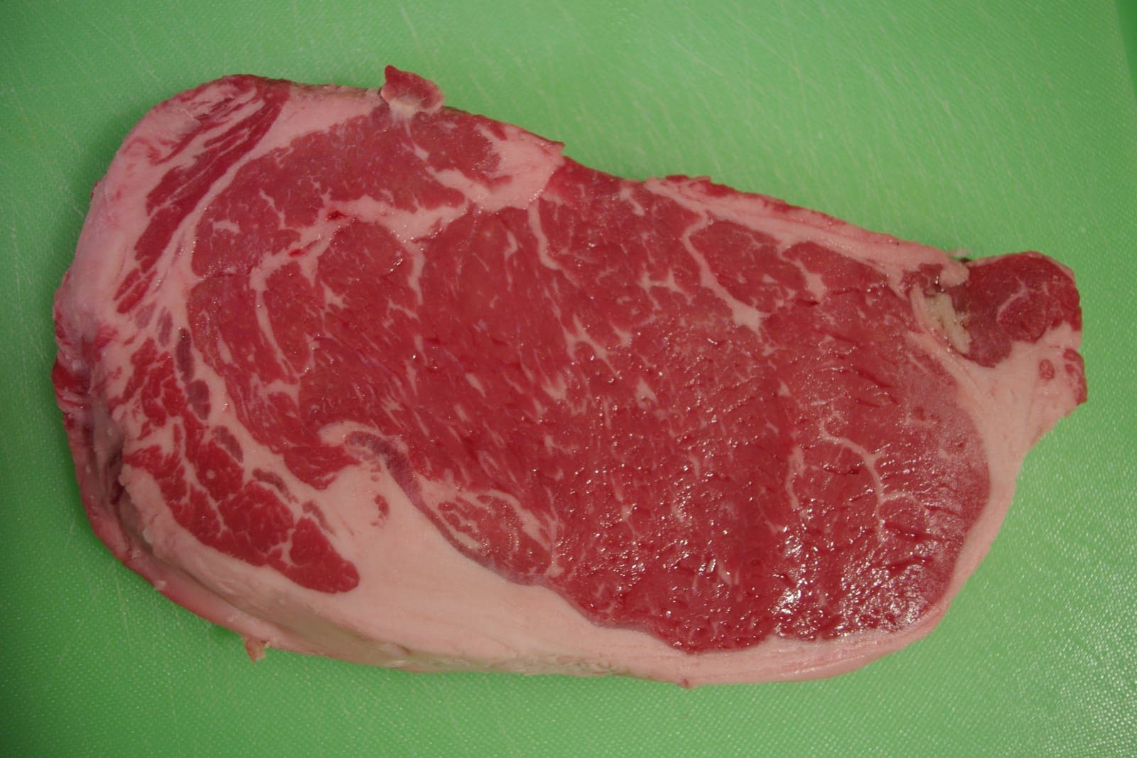A raw marbled steak lying on a green cutting board