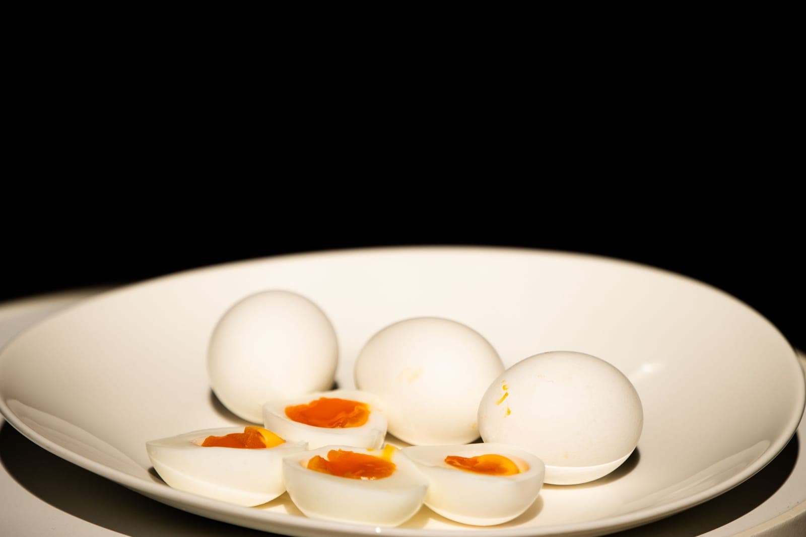 Whole and halved boiled eggs on a white plate, the yolks still deep orange