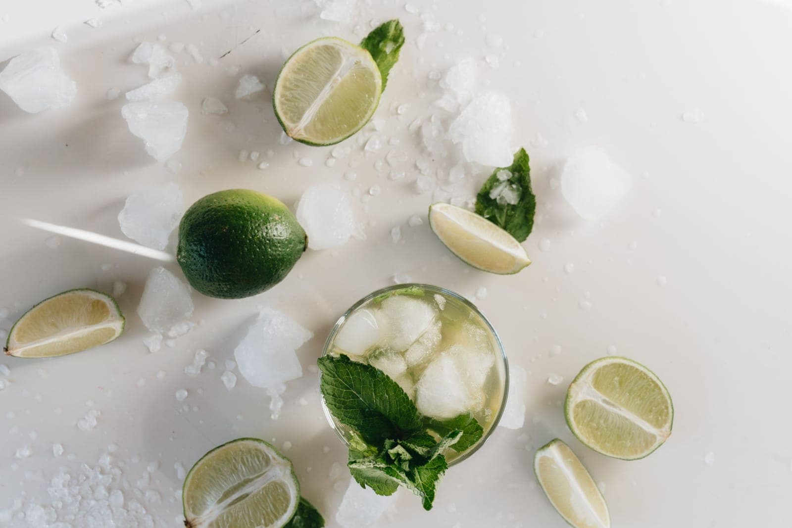 Limes, crushed ice and mint arranged around glasses of a clear iced drink
