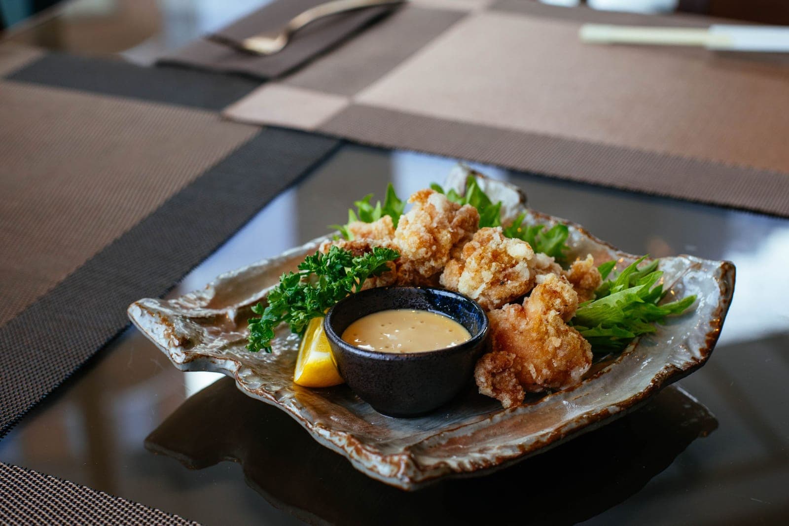 Pieces of crisp fried chicken on a dark plate with a cup of dipping sauce