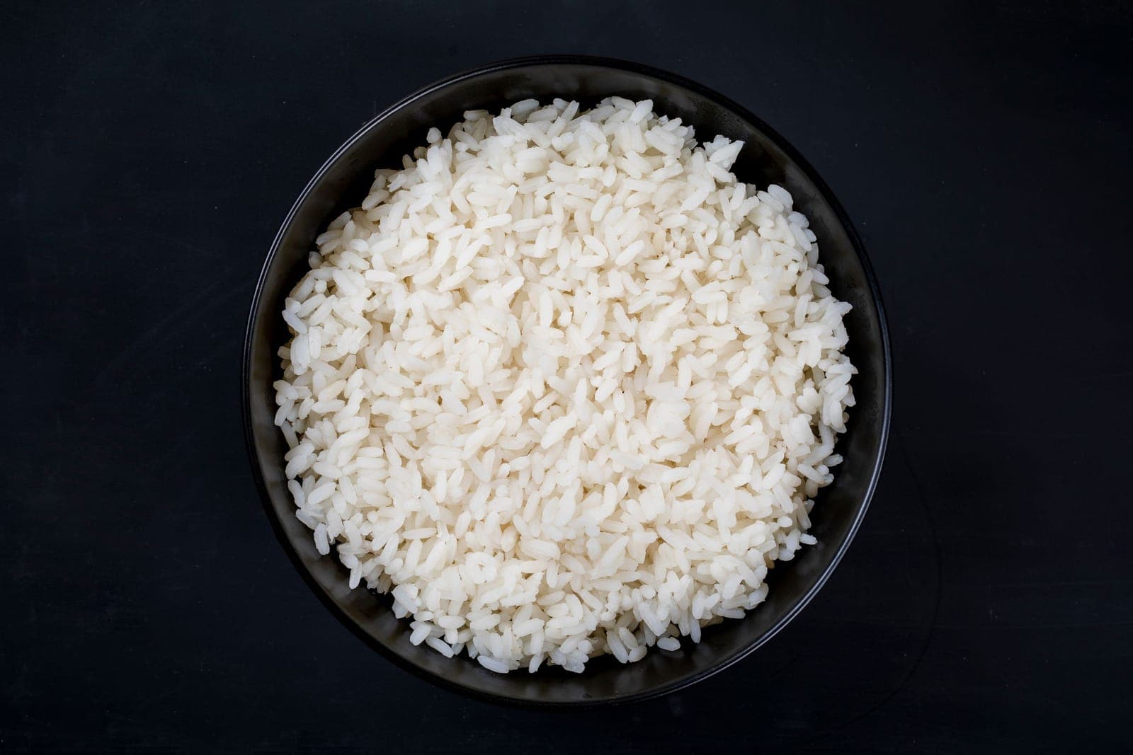 A dark bowl of cooked white rice seen from directly above