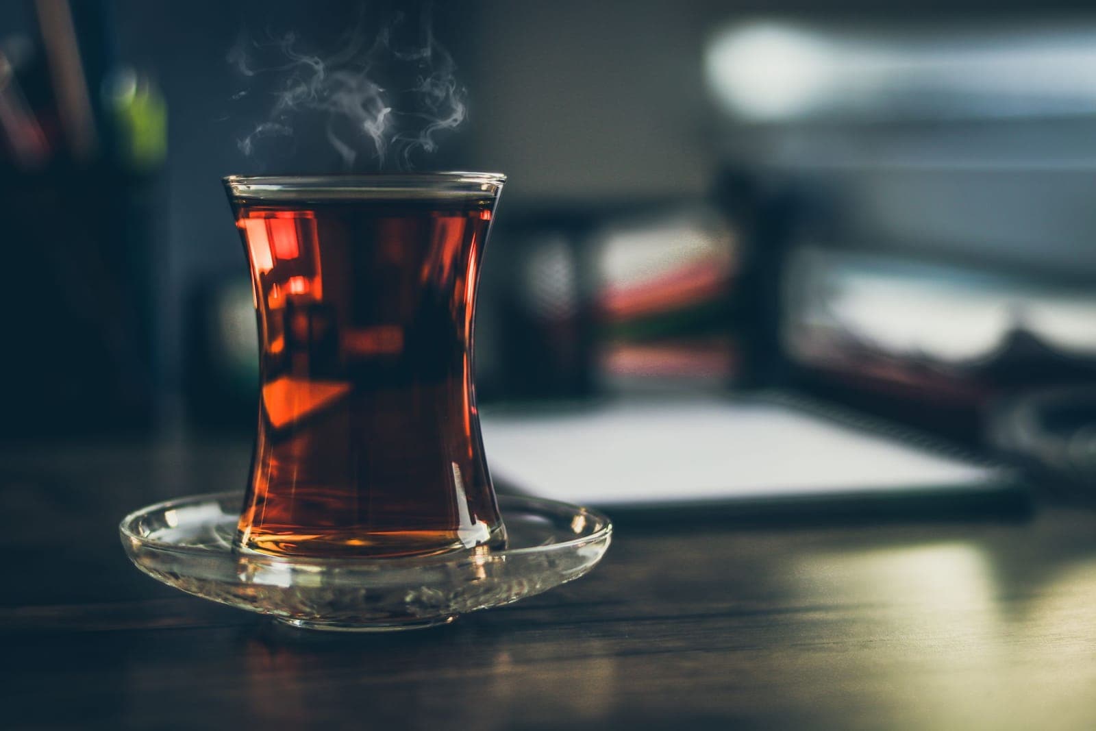 A tulip glass of black tea steaming on a desk