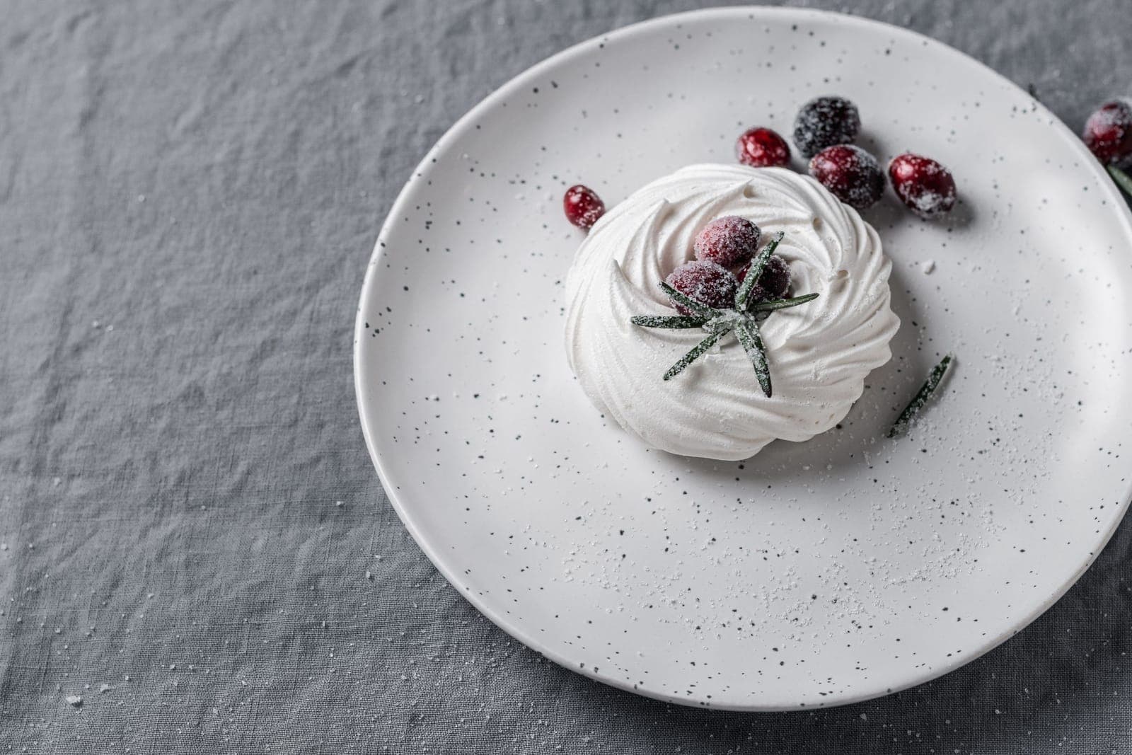 A baked meringue nest topped with sugared cranberries on a speckled plate