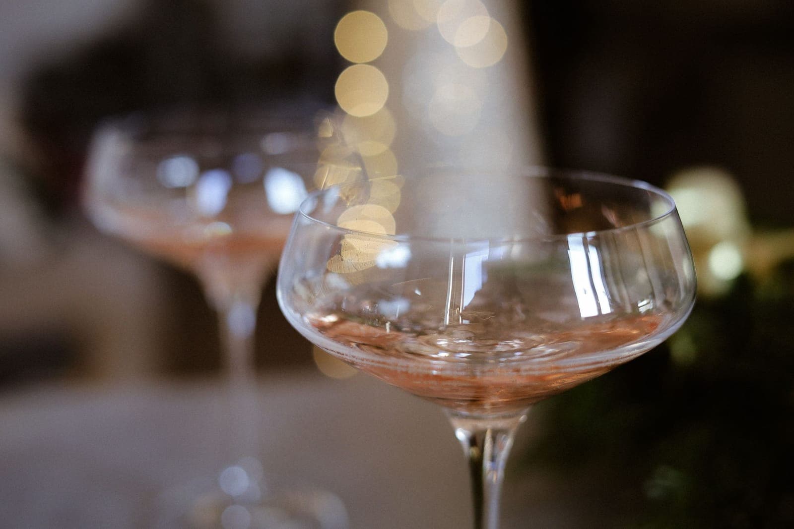 Two coupe glasses holding a pale, clear drink under warm light