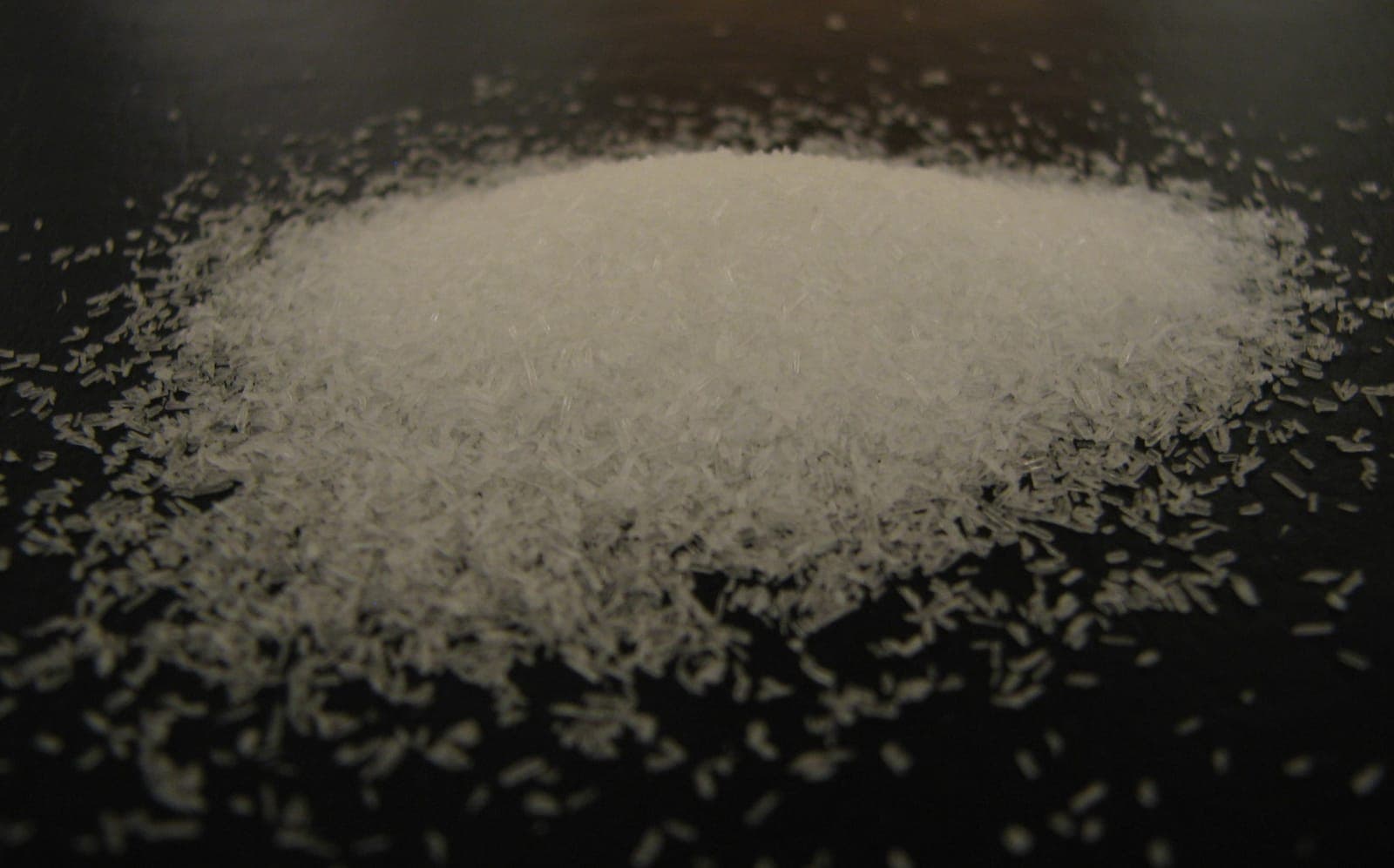 Needle shaped monosodium glutamate crystals scattered on a dark surface