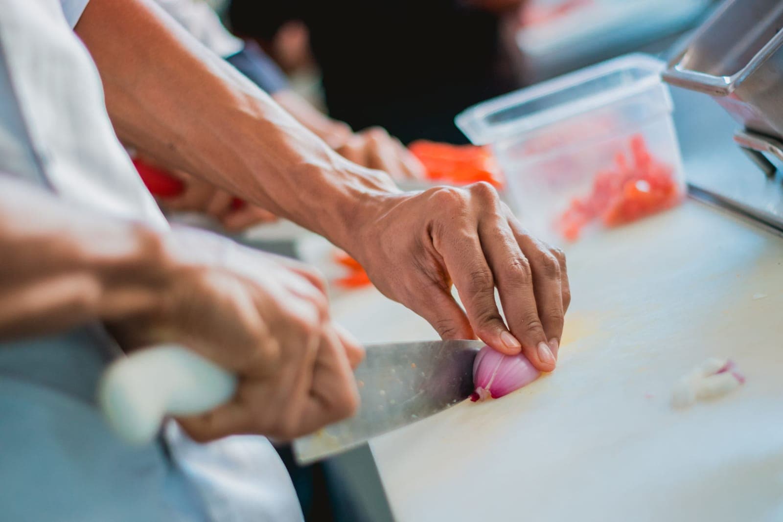 A cook's hands slicing a shallot with a chef's knife on a white board