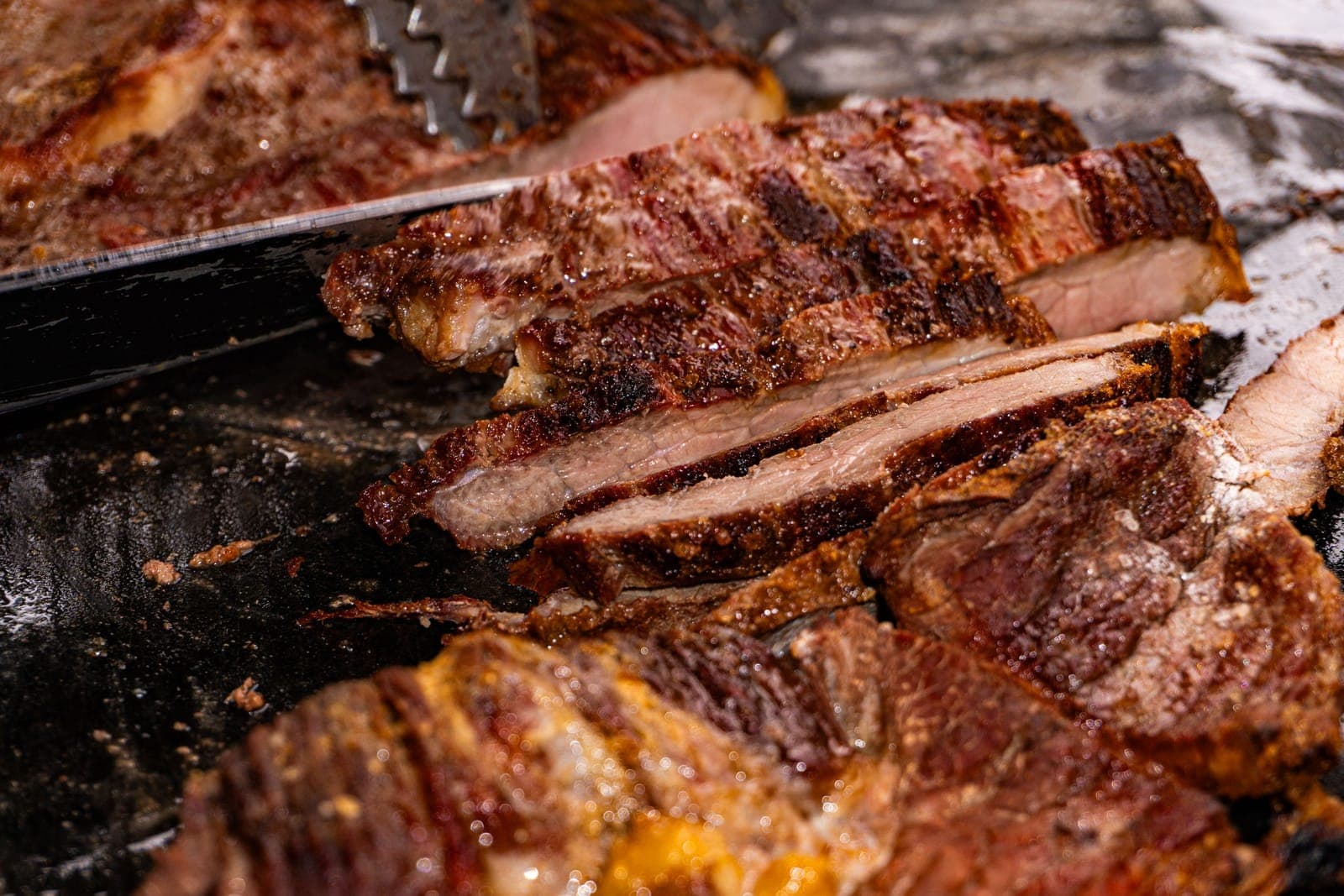 Sliced grilled beef on a griddle with tongs resting beside it
